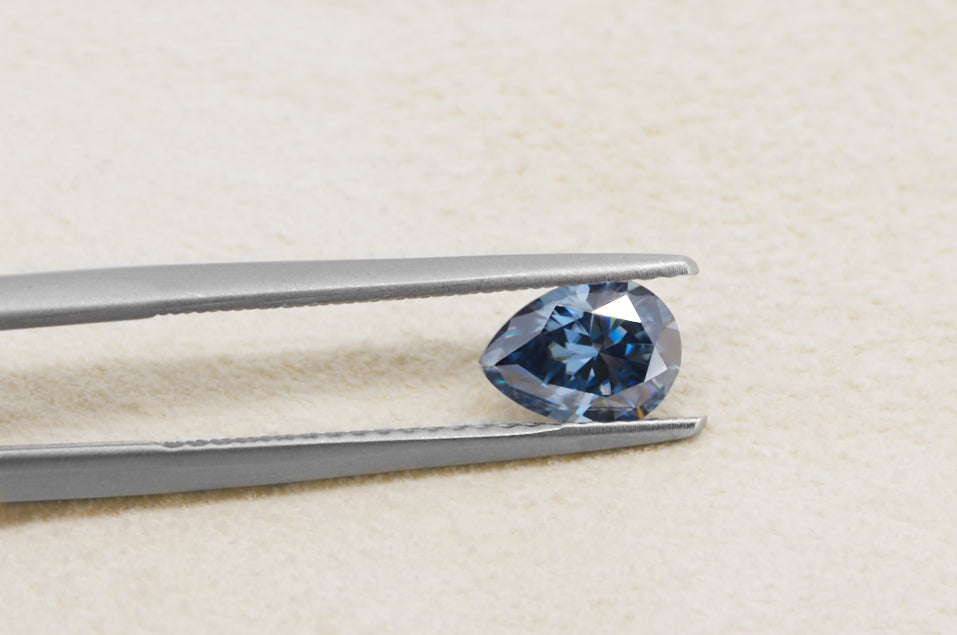 blue pear cut moissanite stone between tweezers on beige fur background