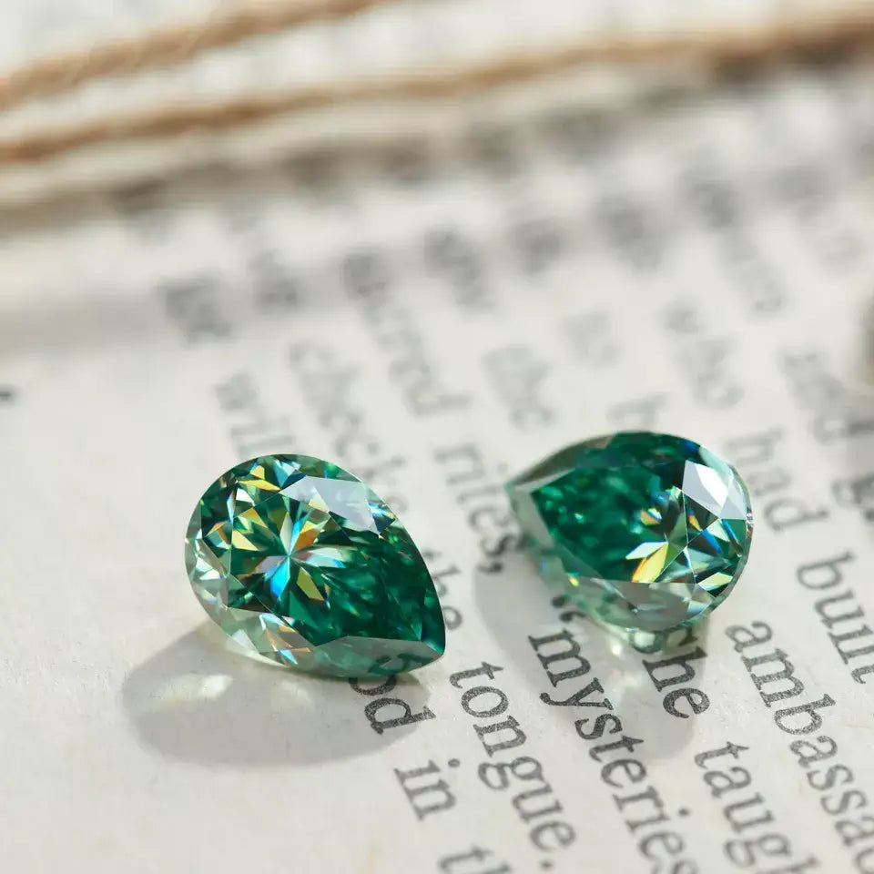 a pair of green pear cut moissanite stones on a book page background