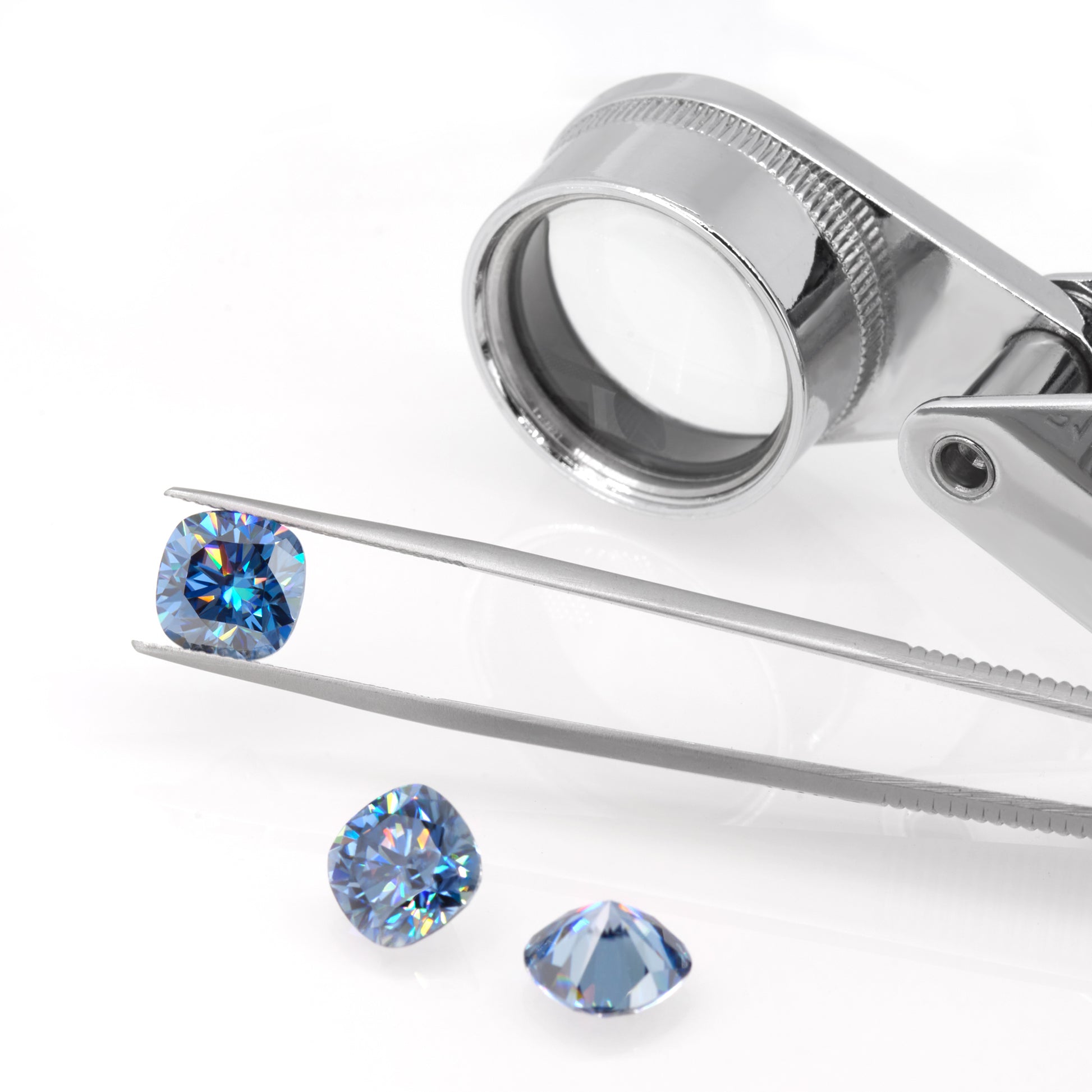 blue cushion cut moissanite stone between tweezers, secondary pair with beautiful internal reflections below it