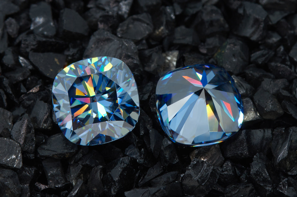 a pair of blue cushion cut moissanite stones on finely crushed black stones, brilliant colorful internal reflections