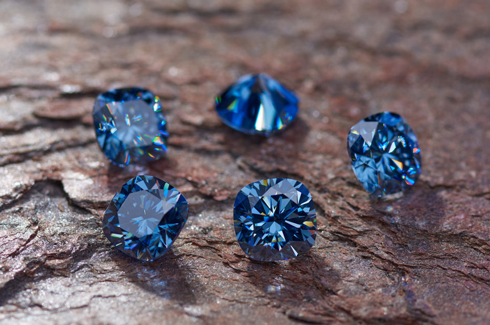 a collection of blue cushion cut moissanite stones on rough rust colored stone surface