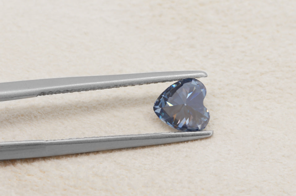 blue heart cut moissanite stone between tweezers on beige fur background