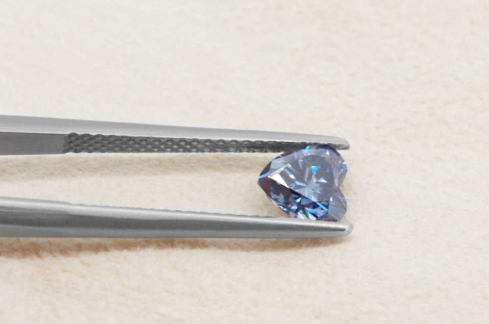 blue heart cut moissanite stone between tweezers on beige fur background