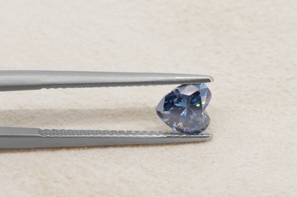 blue heart cut moissanite stone between tweezers on beige fur background