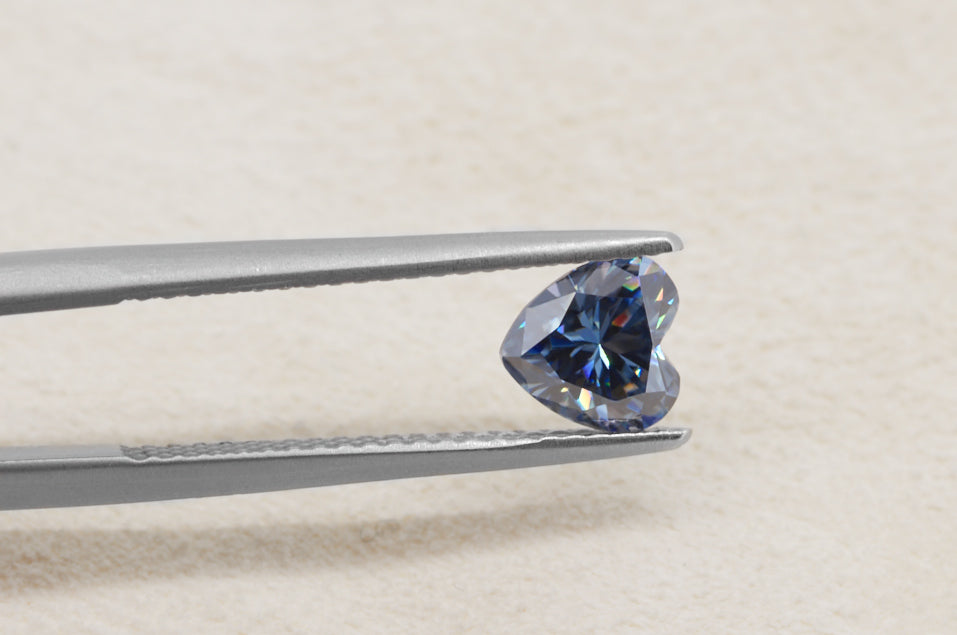 blue heart cut moissanite stone between tweezers on beige fur background, brilliant internal reflections