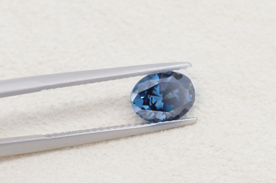 blue oval cut moissanite stone between tweezers on beige fur background