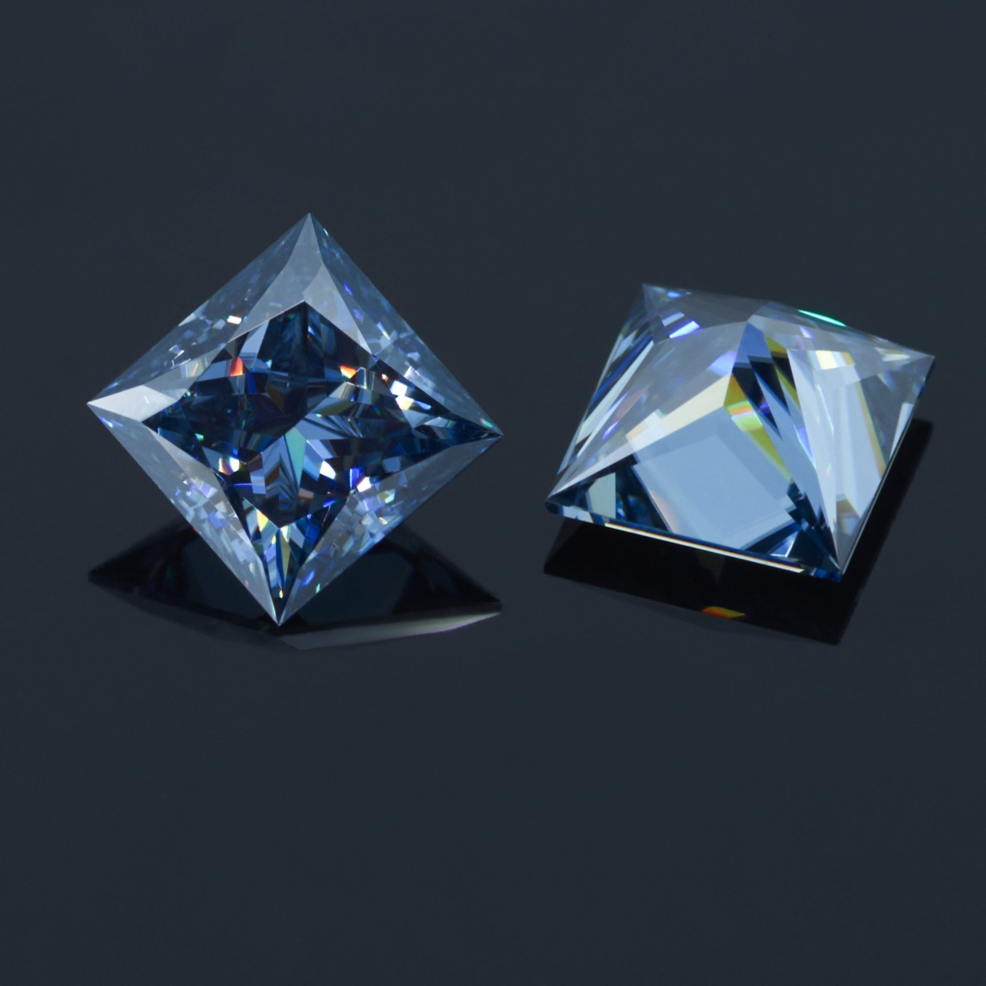 a pair of dark blue princess cut moissanite stones on reflective dark grey background, top and bottom view