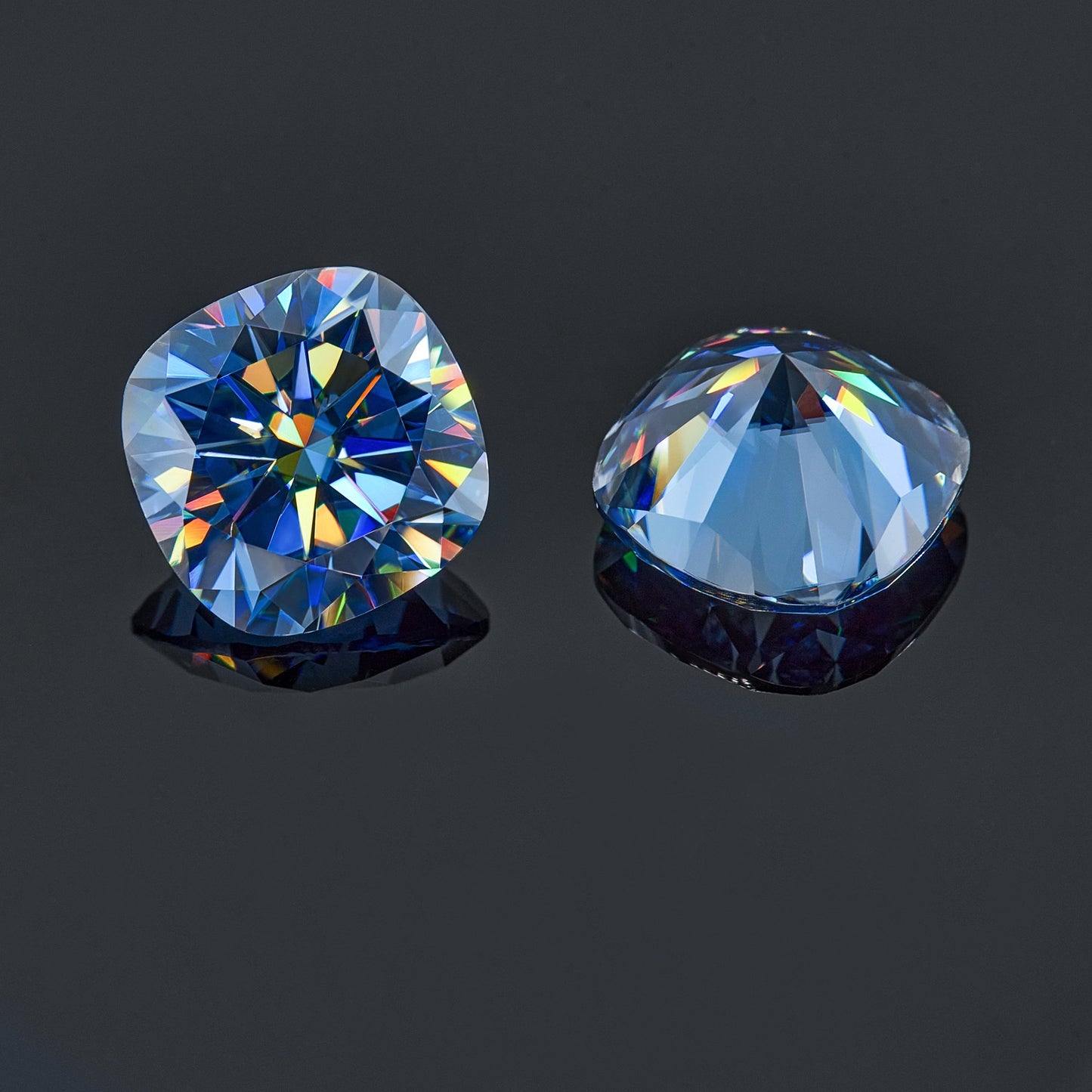 a pair of blue cushion cut moissanite stones on reflective dark grey background, top and bottom view