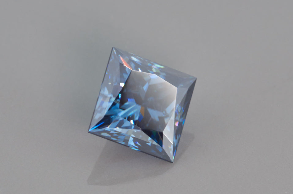 blue princess cut moissanite stone on light grey background, side view 