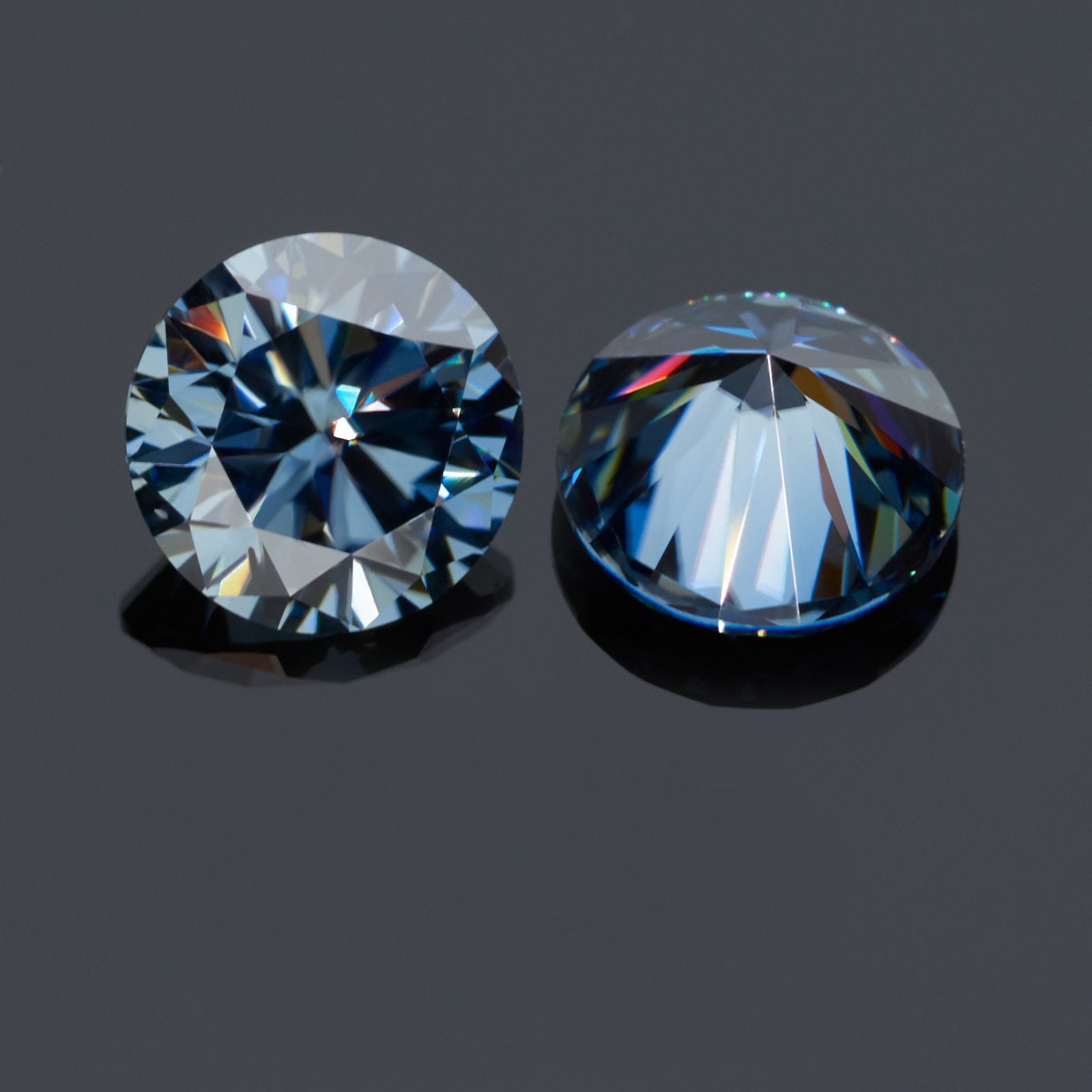 a pair of dark blue round cut moissanite stones on reflective grey background, top and bottom view