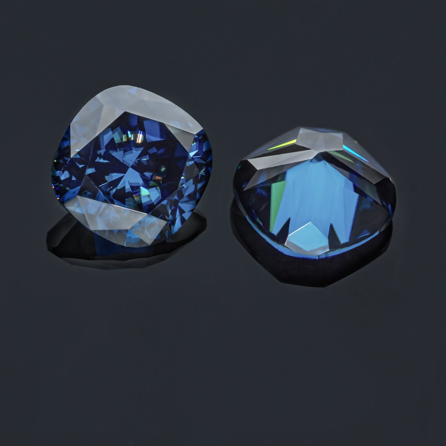 a pair of dark blue cushion cut moissanite stones on reflective grey background, top and bottom view