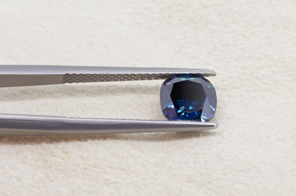 dark blue cushion cut moissanite stone between tweezers on beige fur background