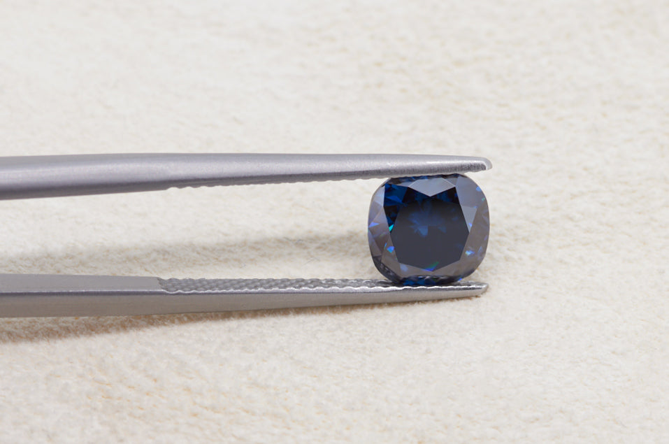 dark blue cushion cut moissanite stone between tweezers on beige fur background