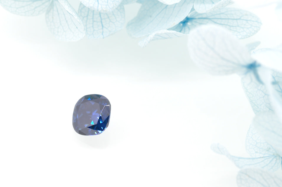 dark blue cushion cut moissanite stone on white background surrounded by white flowers