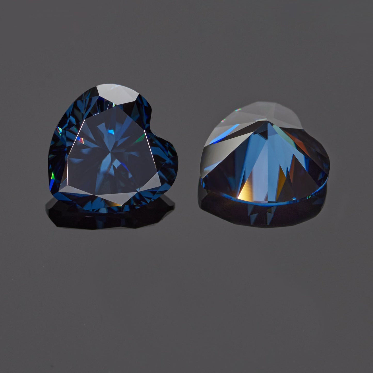 a pair of dark blue heart cut moissanite stones on reflective grey background, top and bottom view