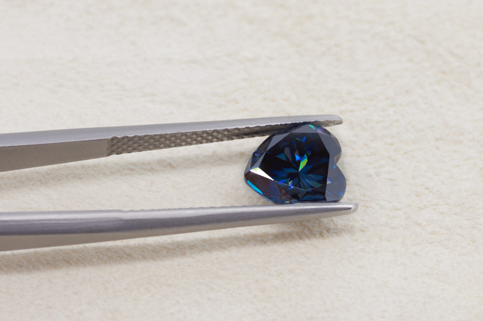 dark blue heart cut moissanite stone between tweezers on beige fur background