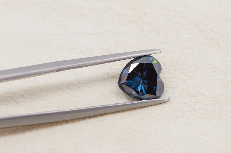 dark blue heart cut moissanite stone between tweezers on beige fur background