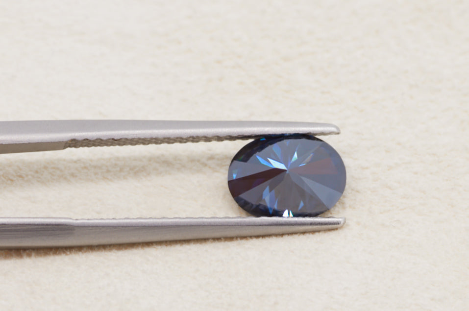 dark blue oval cut moissanite stone between tweezers, back view