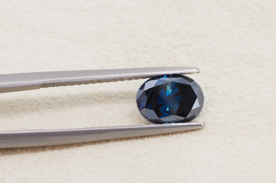 dark blue oval cut moissanite stone between tweezers