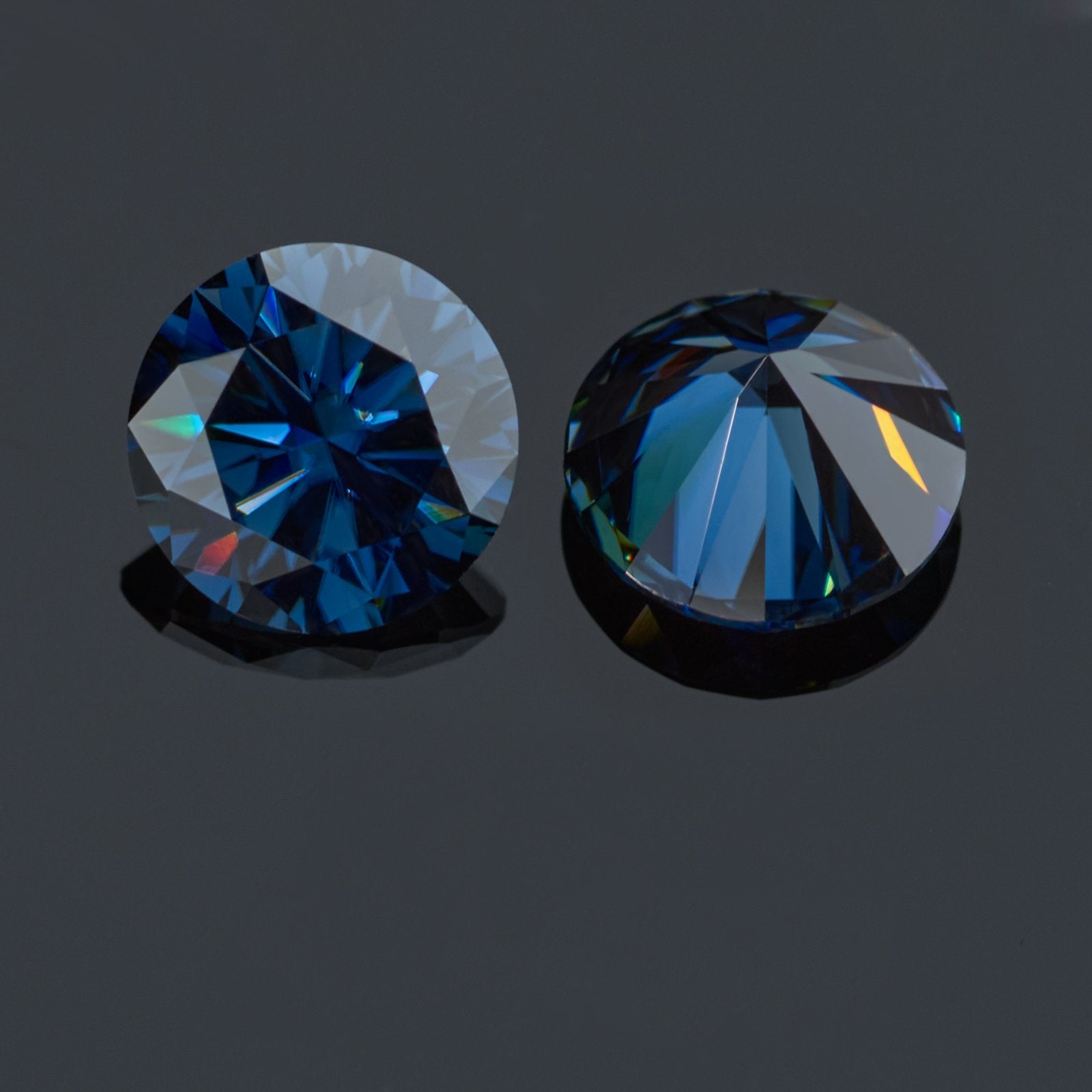 a pair of dark blue round cut moissanite stones on reflective grey background, top and bottom view