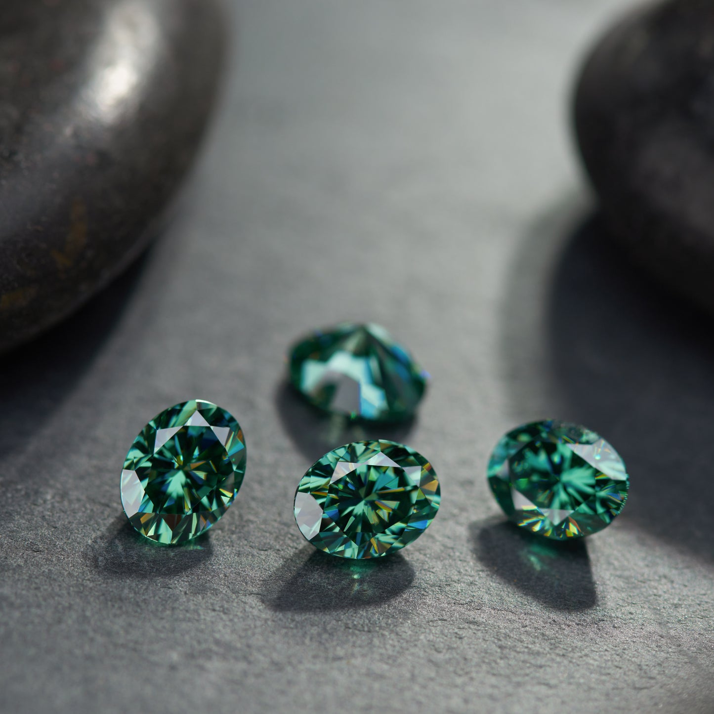 a collection of green oval cut moissanite stones on rough polished dark stone