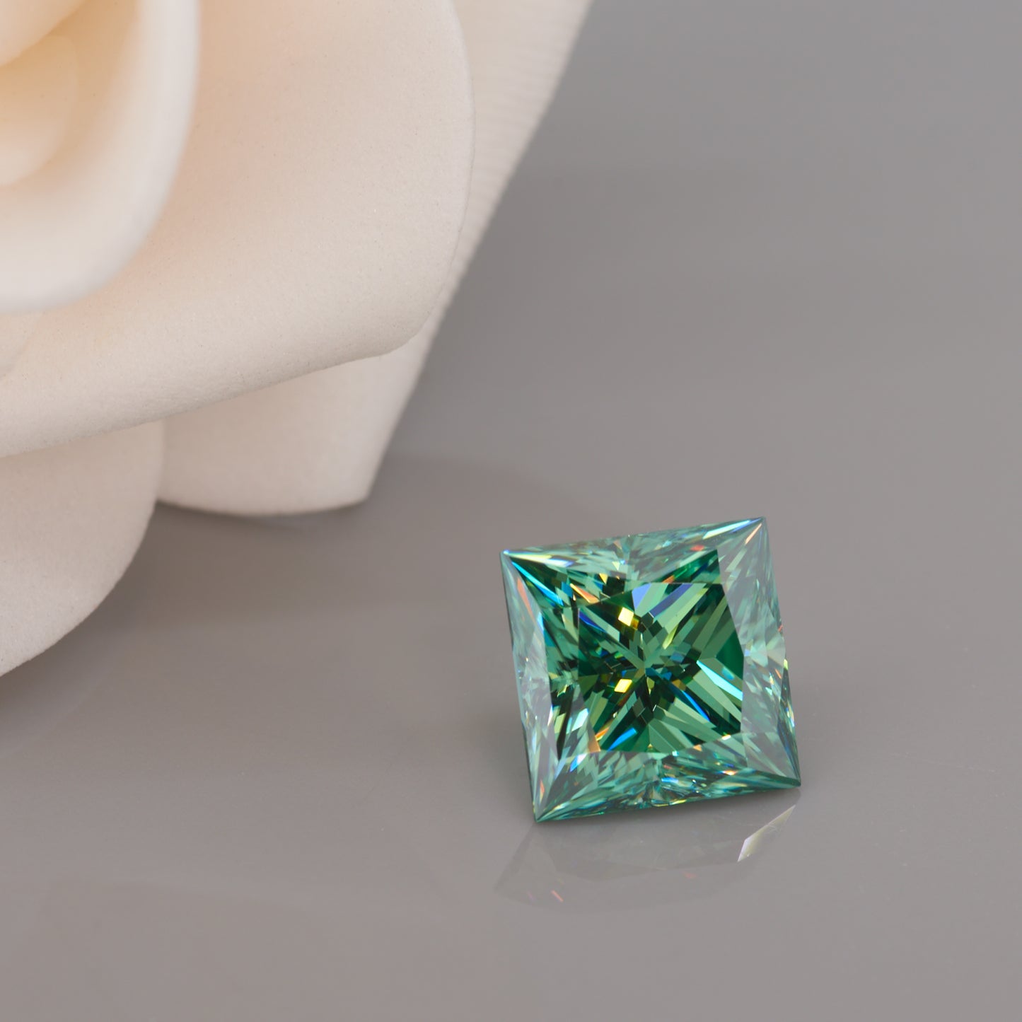 green princess cut moissanite stone on light grey background