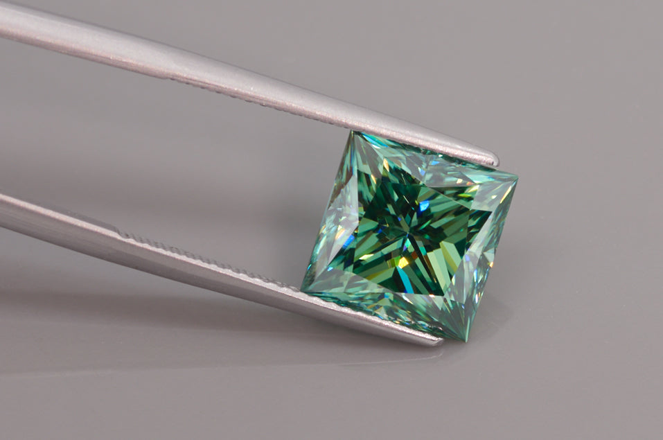 green princess cut moissanite stone between tweezers on light grey background