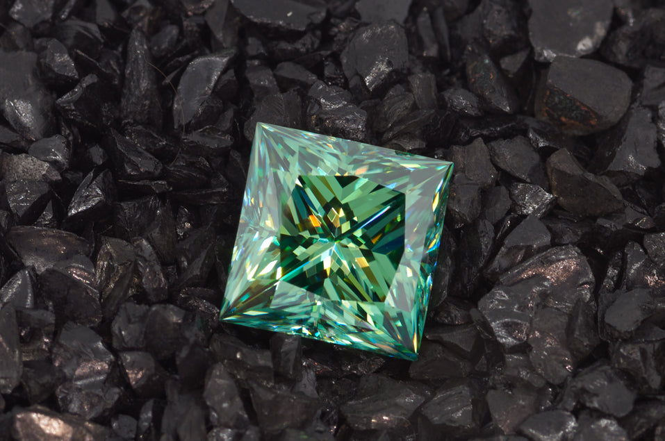 green princess cut moissanite stone on finely crushed black rock, top view