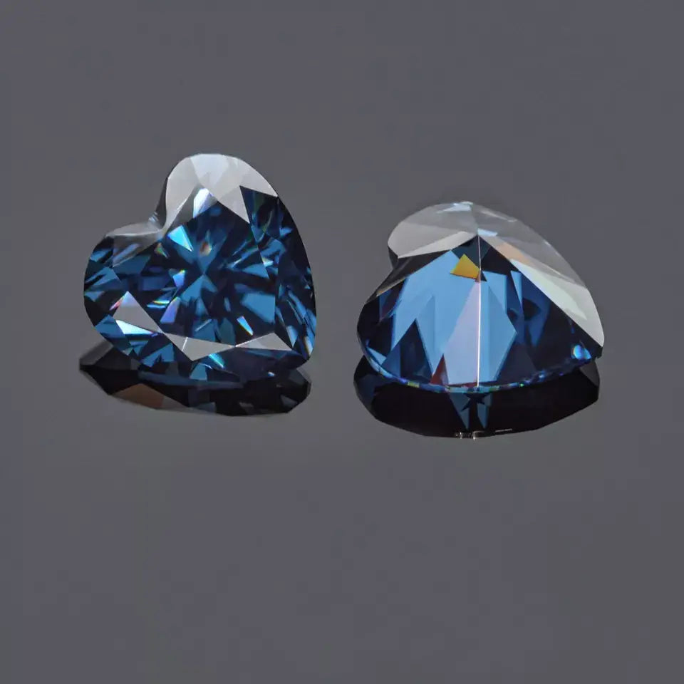 a pair of dark blue heart cut moissanite stones on reflective grey background, top and bottom view