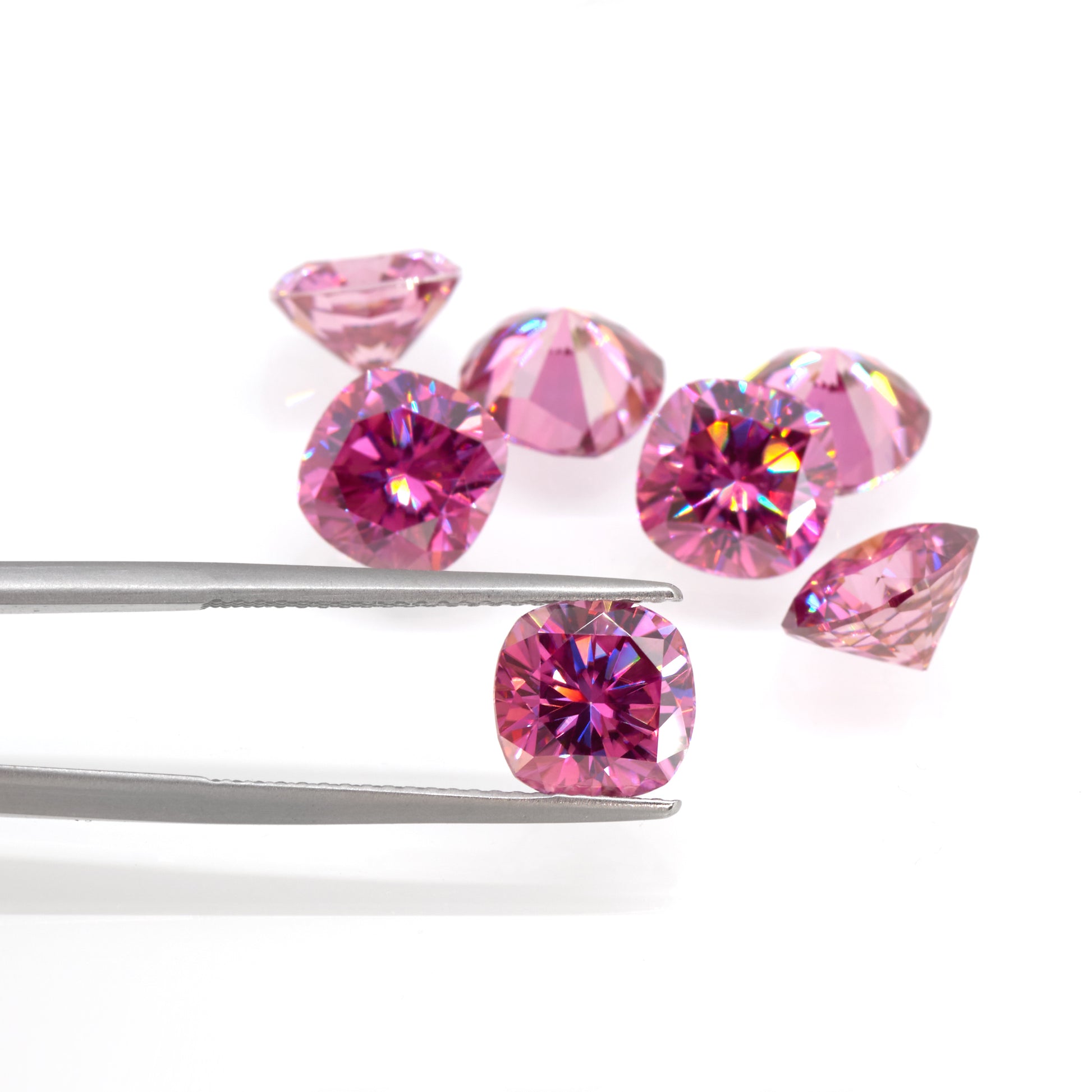 a collection of pink cushion cut moissanite stones on white background, one of them in tweezers