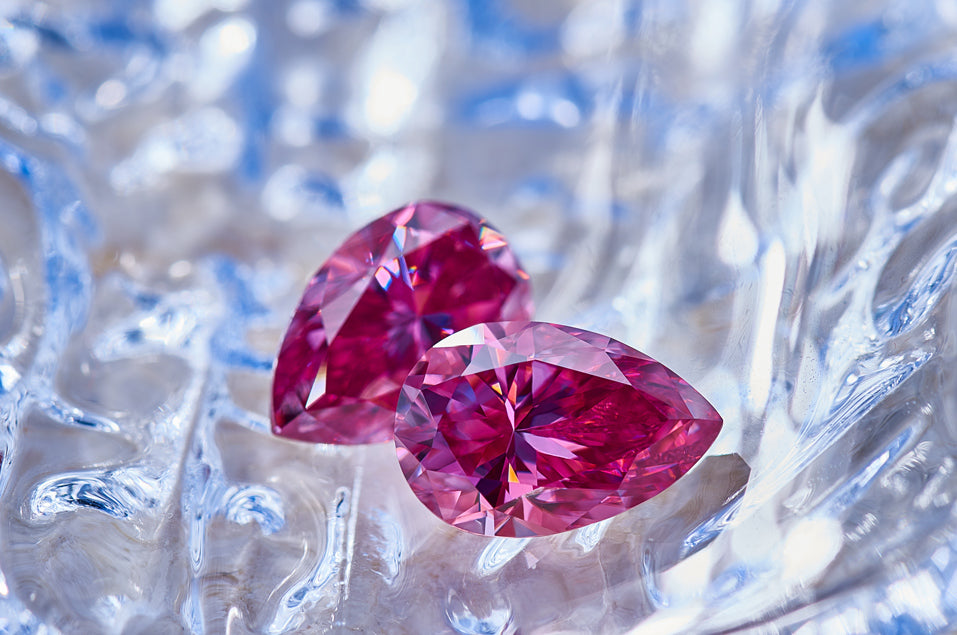 a pair of pink pear cut moissanite stones on reflective background