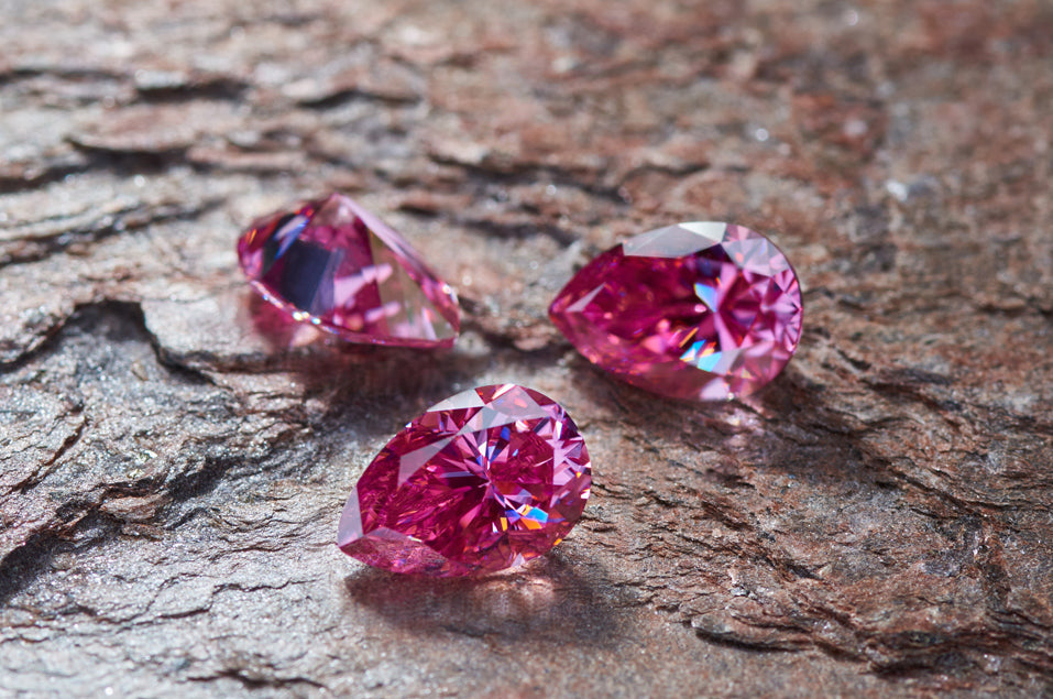 a trio of pink pear cut moissanite stones on stone background