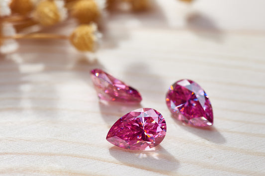 a trio of pink pear cut moissanite stones on light colored wood 