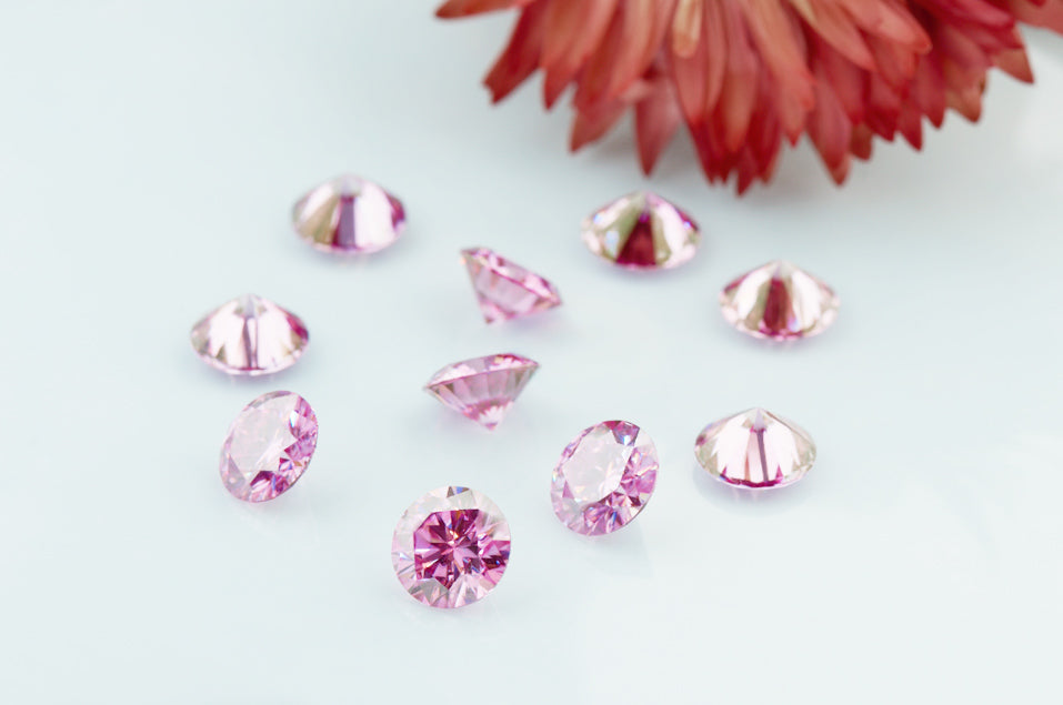 a collection of pink round cut moissanite stones on off white background with a dried flower