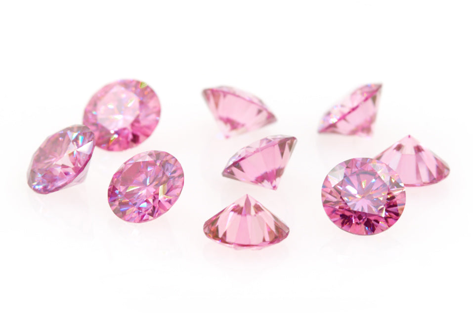 a collection of pink round cut moissanite stones on reflective white background