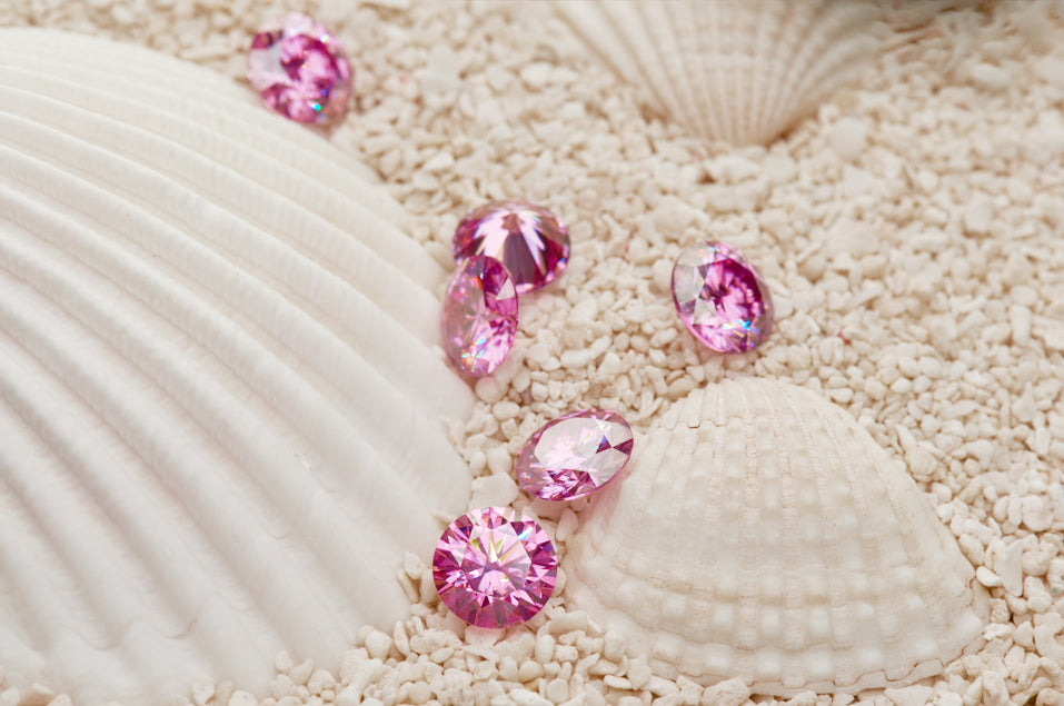 a collection of pink round cut moissanite stones on small stones and sea shells