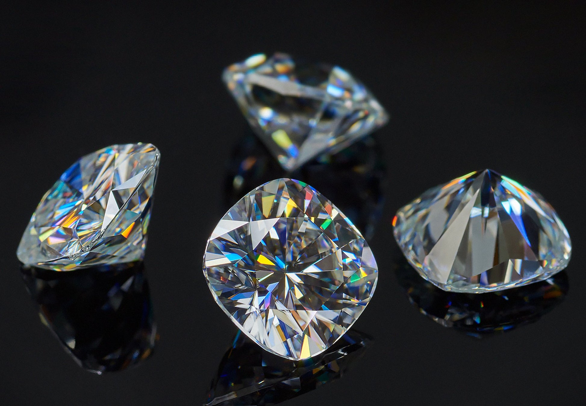 a collection of four white cushion cut moissanite stones on black background