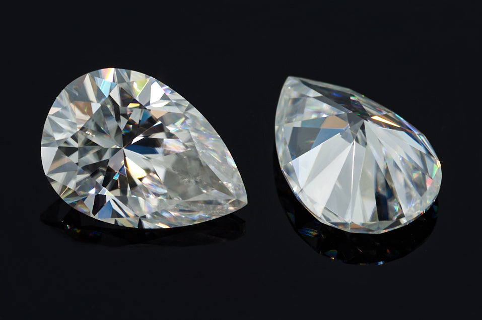 a pair of white pear cut moissanite stones on black background, brilliant internal reflections