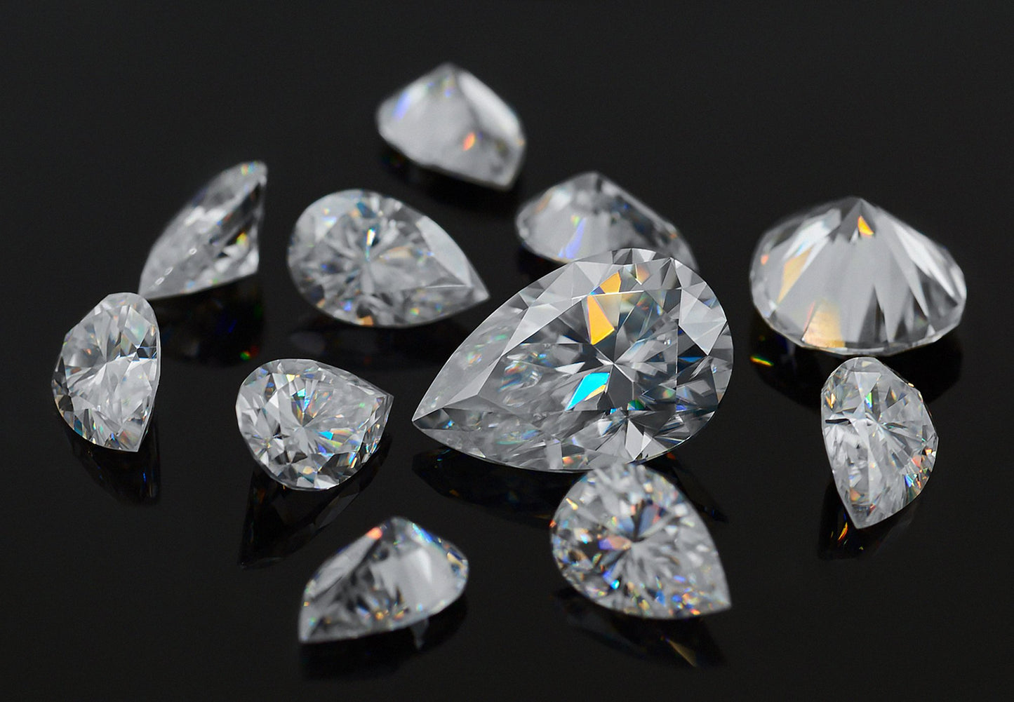 a collection of white pear cut moissanite stone on black background, different sizes