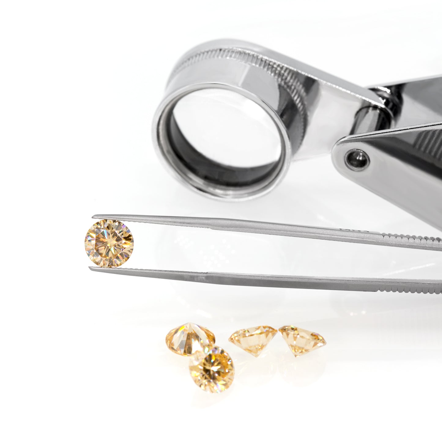 a yellow round cut moissanite stone between tweezers, a magnifying glass and yellow stones under it